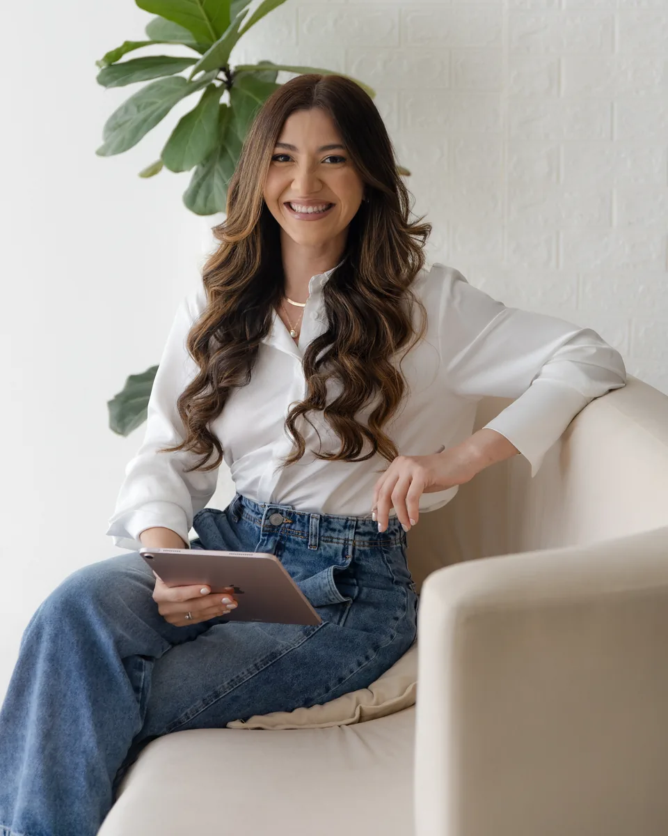 Iara Bianca sorrindo, sentada no sofá com um tablet no colo